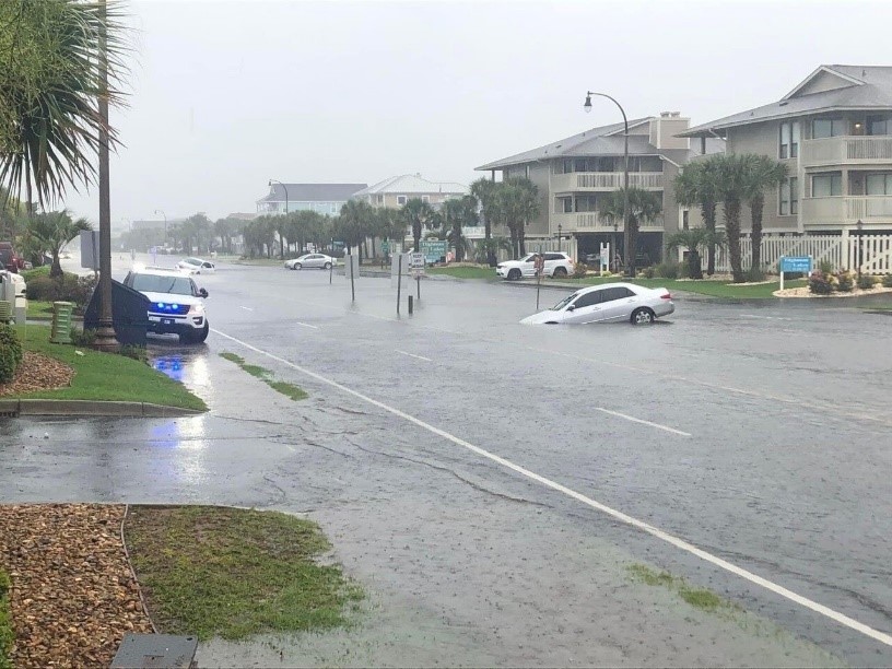 Flooded street along the coast with a car seemingly stuck.